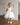 Little girl wearing a luxury white sequin flower girl dress by Aylu Bebe, featuring flutter sleeves and a sparkling tulle skirt, standing in bright modern room. Perfect for weddings, parties and special occasions.