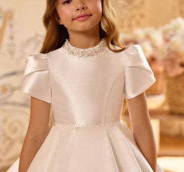 Girl wearing the Isabella Handmade gown in white, standing against a gold floral backdrop, front view