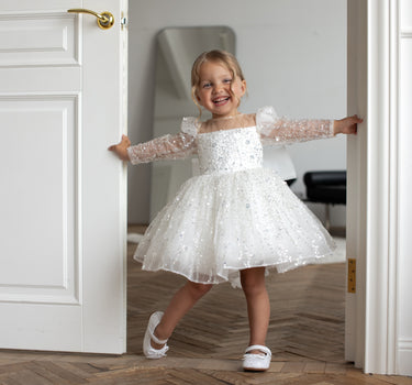 Little girl wearing the Luna sequin Dress standing in a white room showing full front view