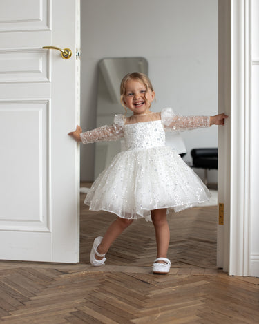Little girl wearing the Luna sequin Dress standing in a white room showing full front view