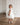 Little girl wearing the Dahlia Blossom white sequin dress by Aylu Bebe, standing on a wooden floor and looking back